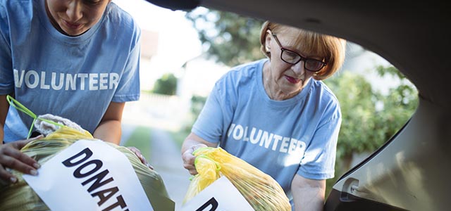 Senior and millennial women unload donation bags from car